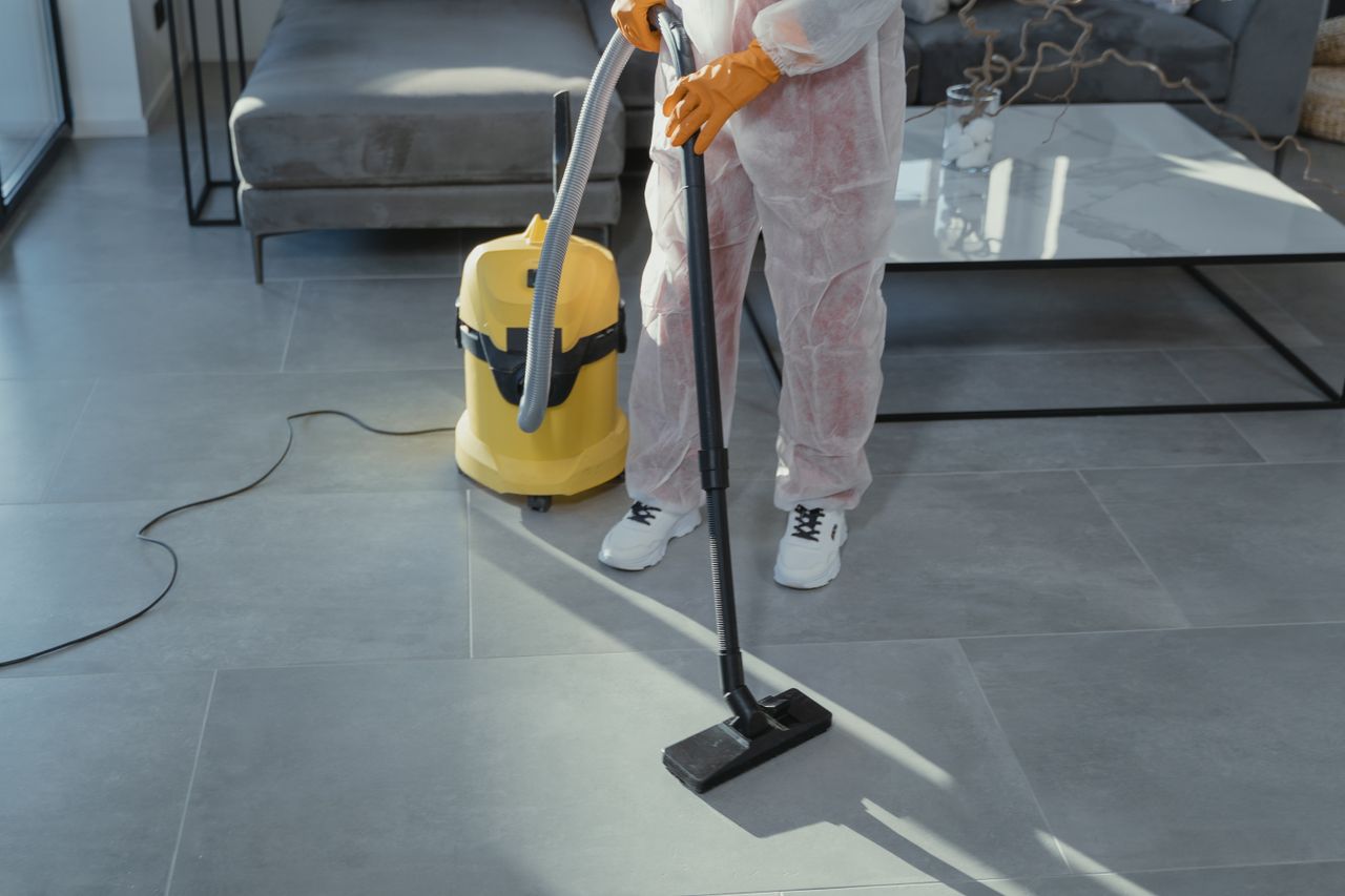 Services A professional cleaner in protective gear vacuuming the floor in a modern living room.